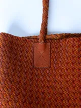 Bolso tipo tote bag color marrón, confeccionado en cuero trenzado. Tiene doble asa de hombro y base rectangular.