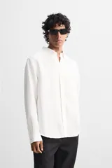 Camisa color arena de lino con cuello abotonado, manga larga con puños abotonados, corte regular y bajo con aberturas laterales.