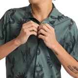 Camisa de manga corta color verde con estampado de cactus, serpientes y soles. Tiene cuello clásico y cierre con botones. Marca Roark, modelo Bless Up Trail.