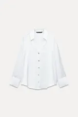 Camisa blanca de satén con cuello solapa, escote en pico, manga larga y cierre frontal con botones.
