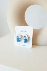 Aros de acero quirúrgico hipoalergénico con forma de argolla plateada y dije circular colgante de piedra natural color azul.