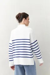 Polera blanca de punto con cuello alto y cierre metálico, de calce relajado y diseño a rayas horizontales azules.