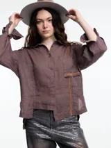 Camisa de manga larga color marrón de lino 100% con calce relajado y diseño asimétrico. El bolsillo delantero está colocado de forma invertida, un detalle lúdico que rompe con lo clásico. Lleva un bordado tipo pespunte en color contraste que recorre el frente y el bolsillo.