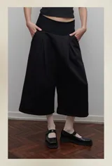 Bermuda sastrera negra confeccionada en felpa con pretina de lycra de algodón, tiro bajo, bolsillos laterales y pliegue delantero de gran tamaño.