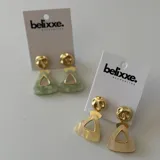 Par de aros colgantes con base redonda dorada y dije triangular con abertura, en color verde y beige.