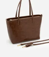 Bolso shopper grande color marrón de material sintético con doble asa, una fija y otra larga desmontable. Tiene cierre de cremallera y detalles de recortes.