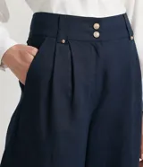 Pantalón pantacourt azul marino de lino y algodón, con cintura alta, pliegues delanteros, bolsillos laterales y cierre frontal con cremallera y botones.