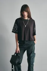 Remera marrón holgada de algodón con escote redondo y mangas al codo. Presenta bordados de canutillos y lentejuelas en las mangas.
