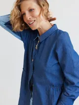Camisa celeste de algodón con cuello clásico, cierre frontal con botones y mangas largas. Presenta volados en el frente y corte evasé.