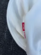 Buzo hoodie color crema con bolsillo tipo canguro y logo de la marca bordado en el frente.