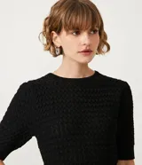 Blusa negra de manga corta con cuello redondo y textura de punto con patrón de corazones o escamas.