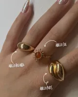 Set de tres anillos dorados de diferentes diseños: uno liso y abombado, otro con forma de sol con una piedra naranja en el centro, y otro con forma orgánica.