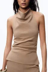 Top color beige de cuello halter y hombros descubiertos, con espalda descubierta, bajo con aberturas laterales y cierre en cuello con botones.