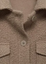 Chaqueta color gris con textura bouclé, cuello camisero, cierre frontal con botones, dos bolsillos de solapa con botón en el pecho y mangas largas.