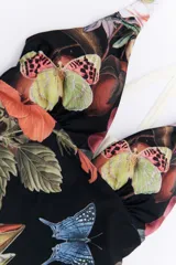 Malla enteriza con estampado de flores, mariposas y aves sobre fondo negro. Presenta breteles finos cruzados en la espalda y ribete color crudo.