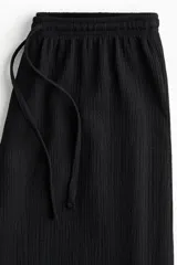 Pantalón negro de punto con cintura elástica y cordón ajustable. Corte holgado con piernas anchas y tiro alto.