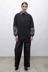 Remerón negro oversize con cuello camisero gris, mangas largas grises con puños elásticos, bolsillo con tapa en el pecho y logo bordado.