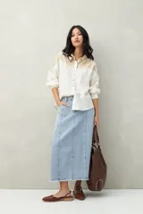 Camisa de lino color crudo y beige, con diseño bicolor y recorte ondulado en el canesú. De silueta relajada, cuenta con mangas amplias y puños camiseros. Se completa con botones de nácar.