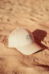 Gorra de gabardina color crudo con visera curva y bordado frontal de una ola con la inscripción "Glassy Waves".