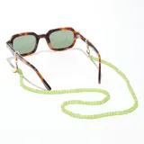 Correa para lentes verde con cuentas acrílicas y terminales de goma transparente. Incluye un dije circular dorado con el logo de la marca grabado.
