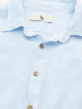 Camisa celeste de lino, de manga larga con botones de coco y parche de la marca.