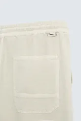 Pantalón color arena de corte recto, confeccionado en tejido de algodón y lino. Cuenta con cintura elástica ajustable con cordón, bolsillos delanteros y traseros de parche.