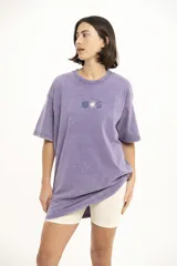 Remera color beige de corte holgado con estampado pequeño de palmera y la letra S en el centro del pecho.