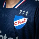 Camiseta de fútbol Umbro del Club Nacional de Football, modelo Away 2, para unisex. Diseño azul marino con detalles en blanco y rojo en cuello y mangas. Incluye logo de Umbro, escudo del club y sponsor Antel en el frente.