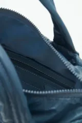 Cartera tote azul de nylon matelassé con diseño de corazones. Tiene manijas cortas y dos correas desmontables, una de cuero sintético y otra de tela trenzada multicolor. Cuenta con cierre superior y dos bolsillos internos.