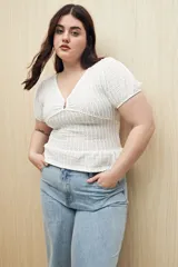 Top blanco con textura tramada, escote en V con leve frunce central, mangas cortas con elástico y volado sutil en el ruedo. Tejido con elasticidad.