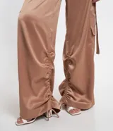 Pantalón wide leg de textura acetinada color café, con bolsillos cargo con solapa en los laterales y tira con moña en los bolsillos y en la barra. Cintura con trabillas y cierre por botón y cremallera.