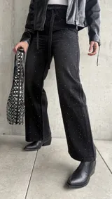 Pantalón de jean negro de corte recto, con tachas plateadas y cinturón fino con hebilla metálica.