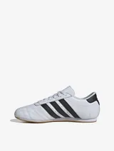 Zapatillas Adidas de cuero blanco con las tres tiras laterales en negro y suela de goma color caramelo.