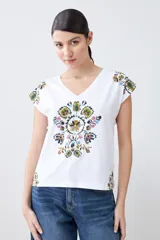 Remera blanca de algodón con escote en V y estampado floral en el frente y los hombros.