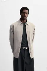 Camisa color crema de corte relaxed fit, confeccionada en tejido de mezcla de algodón suave al tacto. Tiene cuello solapa, manga larga con puños abotonados, un bolsillo de parche en el pecho y cierre frontal con botones.