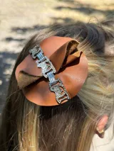 Accesorio para el cabello hecho de cuero en color camel, con diseño circular y detalles decorativos.
