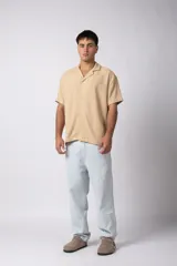 Camisa de manga corta color crudo, confeccionada en lino texturizado. Tiene cuello tipo cubano, cierre frontal con botones y corte recto.