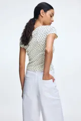 Remera blanca con estampado de flores pequeñas en negro, escote cuadrado y tapeta de botones. Corte entallado y mangas cortas.