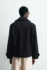 Abrigo corto azul marino de corte relajado, confeccionado en tejido con lana. Tiene cuello con solapas de pico, mangas largas con puños ajustables con trabilla, bolsillos de solapa en la cadera, bolsillo interior, abertura en el centro de la espalda y cierre frontal con botonadura.