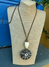 Colgante con cordón de cuero marrón ajustable, cuenta con cuentas de madera y hueso. El dije principal es circular, de color negro y blanco con diseño de espiral.