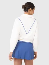Polerón blanco de corte holgado, con cuello polo y cierre de media cremallera. Presenta detalles de ribete azul en el cuello y el cierre.