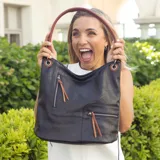 Cartera tipo hobo de color negro confeccionada en símil cuero con detalles calados. Posee apertura superior con cierre, dos bolsillos frontales con cierres metálicos y tiradores decorativos, y un bolsillo posterior con cierre. Incluye una correa corta fija para el hombro en color marrón y una correa larga adicional, desmontable y regulable.