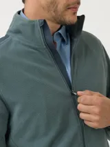 Campera polar celeste de poliéster reciclado con aplicaciones de tela canvas de algodón en los hombros, dos bolsillos frontales con cierre, bolsillos internos, cuello alto y cierre completo.