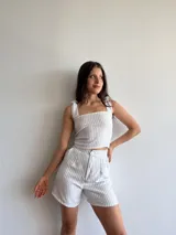 Conjunto de top y short a rayas verticales azules y blancas. El top es musculosa con breteles con volados y el short es de tiro alto con botón.