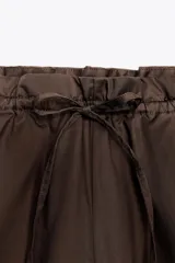 Pantalón marrón tipo barrel, de tiro medio con cintura elástica ajustable con lazada, bolsillos laterales y falsos bolsillos de vivo en la espalda.