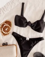 Conjunto de bikini negro texturizado, compuesto por un corpiño con nudo central, breteles anchos y cierre en la espalda, y una bombacha vedetina con nudos en los laterales.