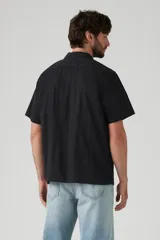 Camisa de manga corta negra con botones blancos y cuello cubano. Tiene un bolsillo en el pecho izquierdo con el logo de Levi's en rojo.