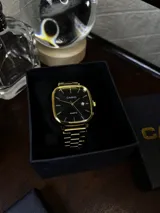 Reloj Casio Quartz dorado con caja cuadrada, dial negro y pulsera de eslabones.