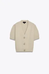 Chaqueta color beige de punto con escote pico y manga corta. Cierre frontal con botones en forma de estrella.