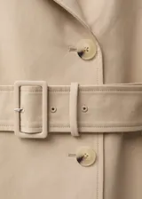 Abrigo largo color beige con cuello con solapa, doble botonadura, cinturón con hebilla, trabillas en hombros y cintura, y abertura posterior en el bajo.